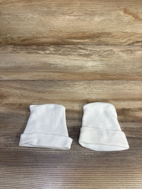 Top-down view of two white preemie fold-over baby hats showcasing rolled cuffs on wood background