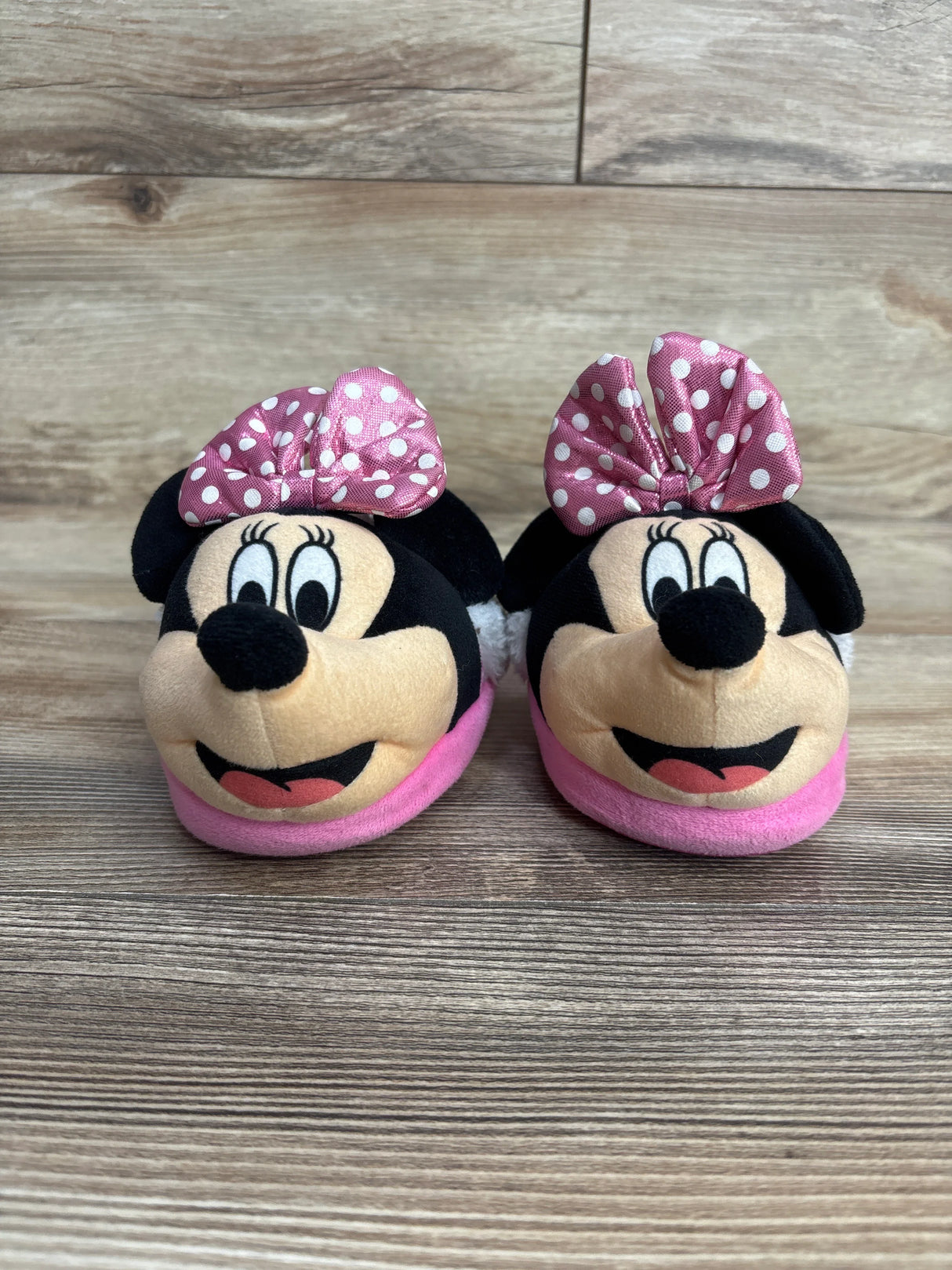 Pair of pink Minnie Mouse baby slippers with polka dot bows on wooden floor