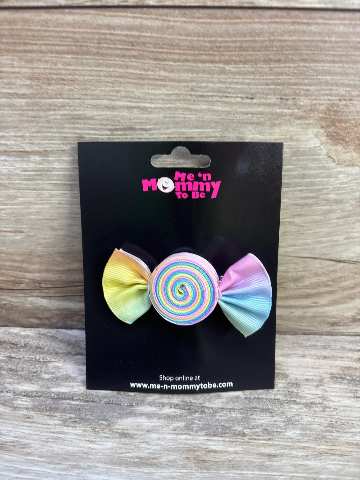 Front of Candy Hair Bow with rainbow spiral center and pastel ribbon ends on black card over wood background