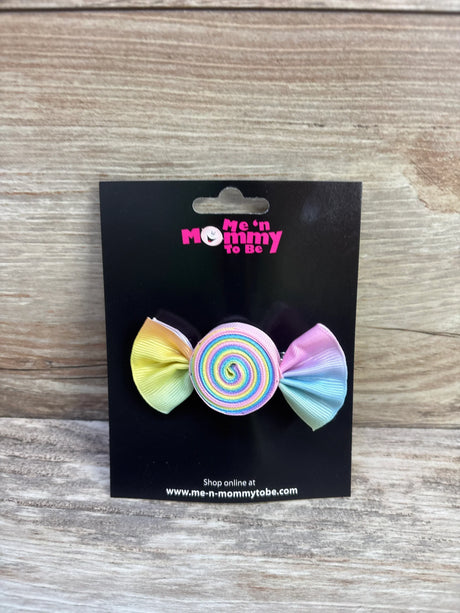 Front of Candy Hair Bow with rainbow spiral center and pastel ribbon ends on black card over wood background