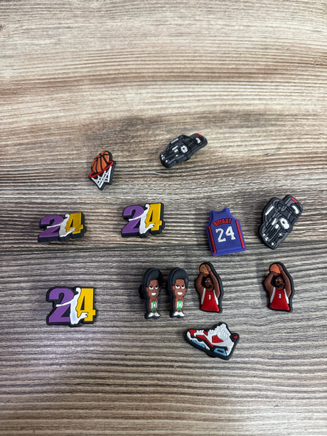 Top view of Basketball Theme Croc Jibbitz Charms showcasing basketball, jersey, shoe, and number 24 designs on a wood-grain background