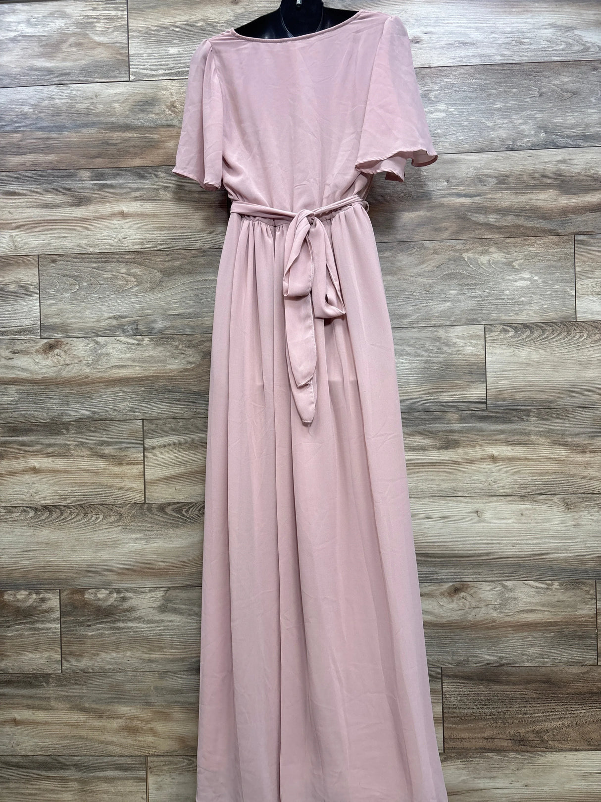 Front view of Baltic Born maternity maxi dress in blush with flutter sleeves, waist sash and long skirt on wood background