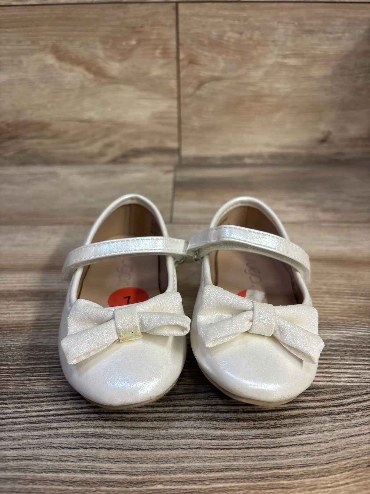 Front view of Sugar Nira white toddler flats showcasing glitter bows and Mary Jane strap on wood floor