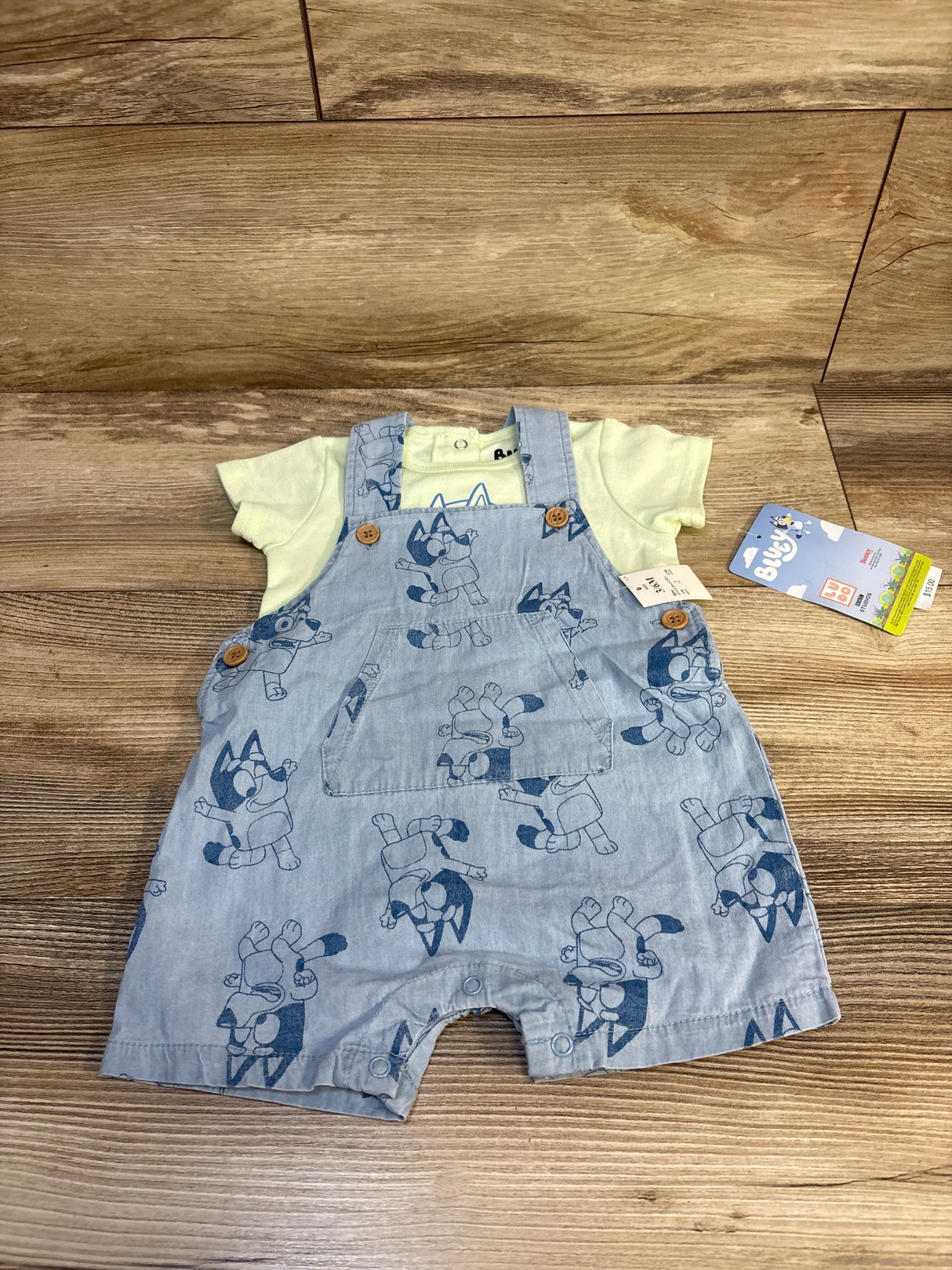 Bluey print denim baby romper with short sleeves, wooden buttons, laid on wood background