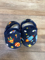 Top-down view of navy baby slippers size 5C showing plush fabric with colorful rocket and planet print and Velcro strap on wood floor