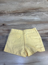 Back view of Janie and Jack yellow toddler shorts showing elastic waistband and faux back welt pockets on wooden surface