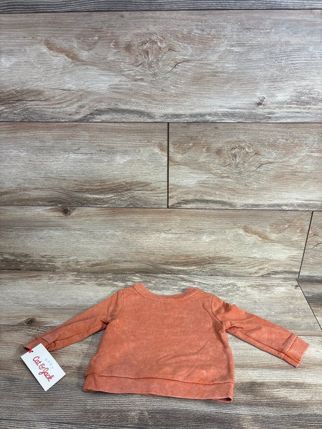 Coral long sleeve baby shirt with tag, laid flat on wood background