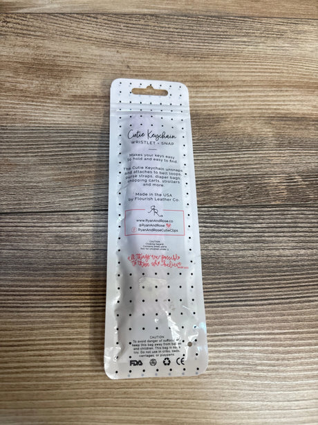 Top-down view of Cutie Keychain wristlet in retail packaging showing black polka-dot design and product information on a wooden surface