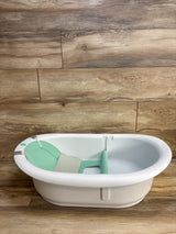 White baby bathtub with mint green support, ideal for newborns and infants, on wood floor
