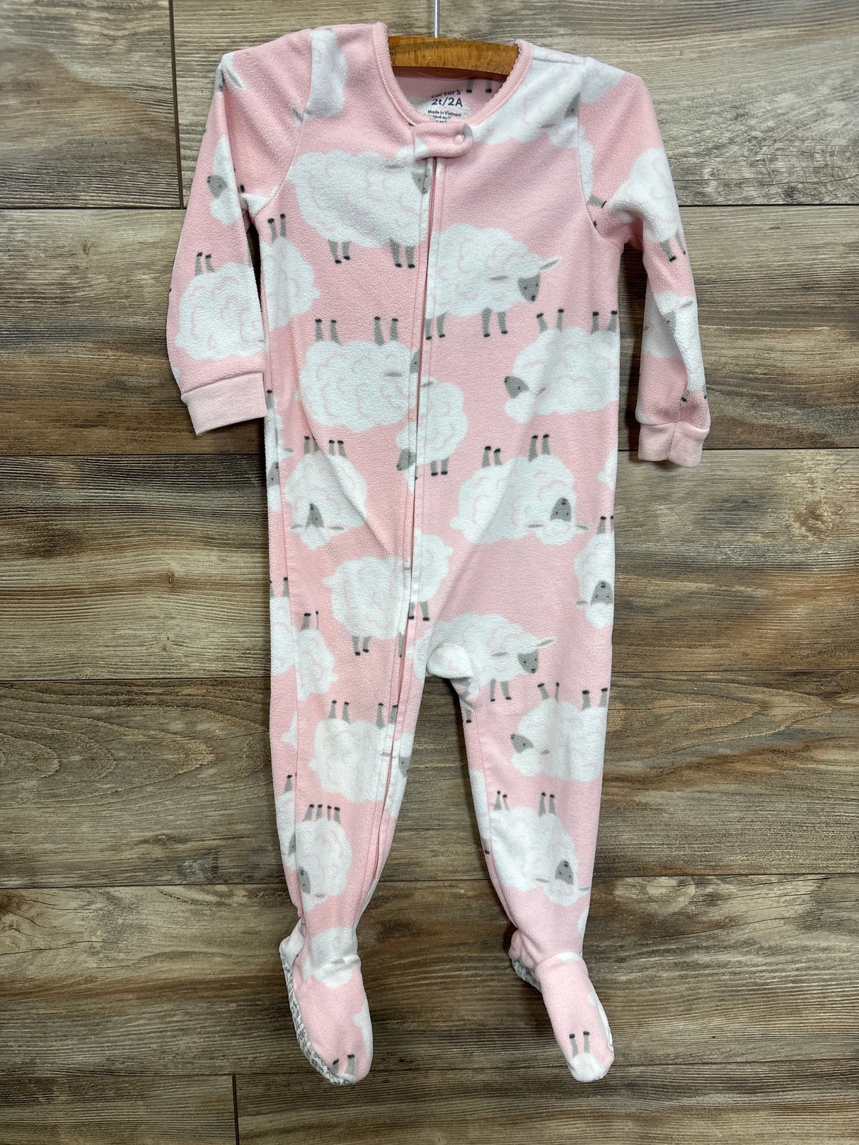 Pink fleece baby sleeper with white sheep print and zipper on wooden floor
