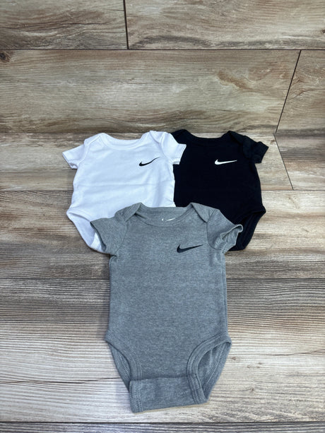Top view of Nike three-pack baby bodysuits in white, black, and gray, size 3 months, on a wood floor