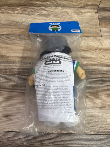 Front view of the Feelings and Emotions washable Sad Doll in clear packaging on a wood floor