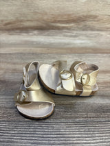 Gold baby sandals with buckle straps on wooden surface, children's footwear