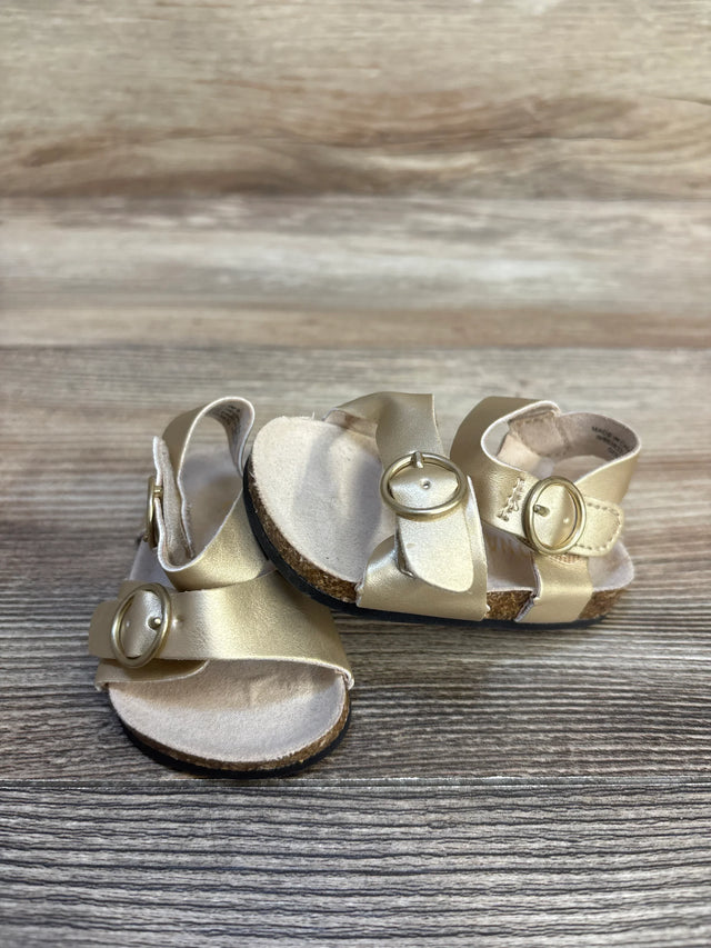 Gold baby sandals with buckle straps on wooden surface, children's footwear