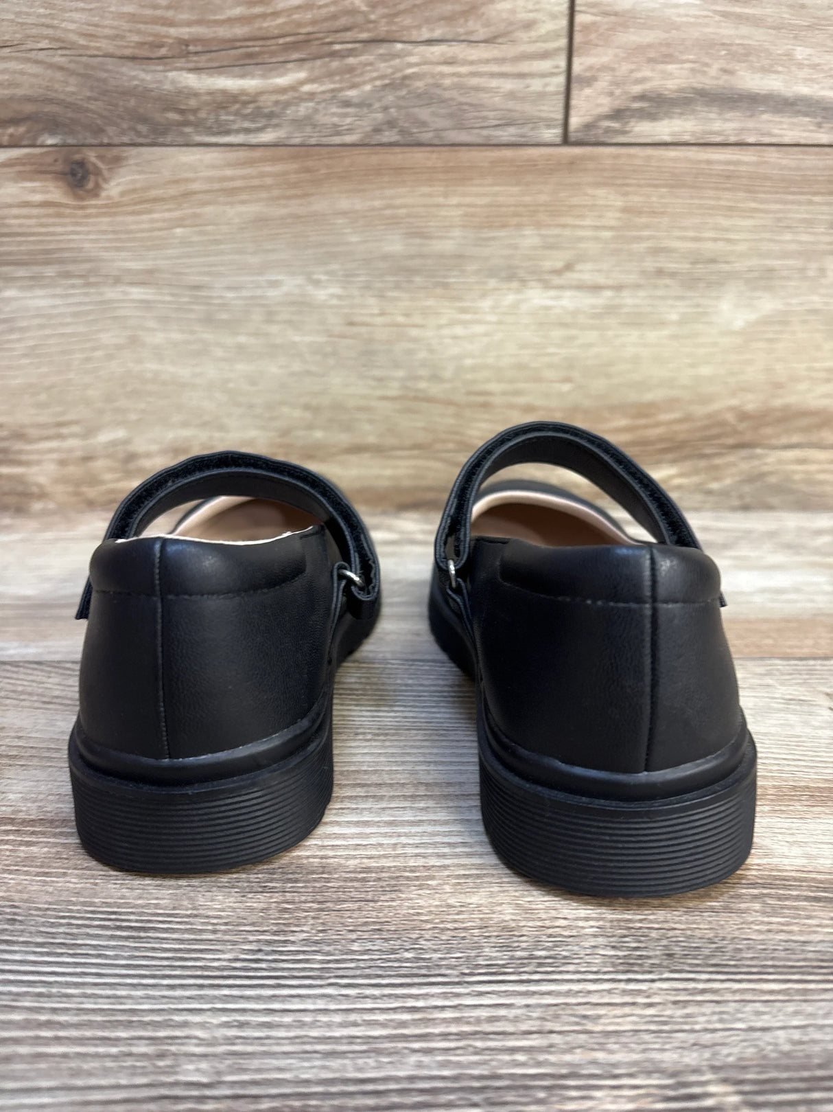 Rear view of black children's dress shoes with velcro straps on wooden floor
