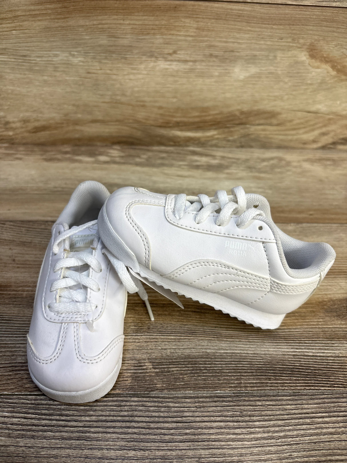 White Puma Roma toddler sneakers with laces on wood background, gently used kids shoes