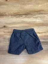 Front flat lay of blue chambray Jumping Beans baby shorts showing elastic waistband and side pockets on wood background