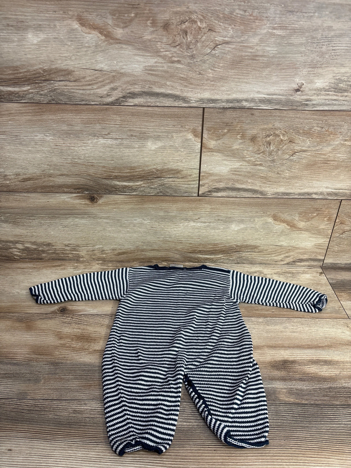 Striped black and white baby knit romper with long sleeves on wooden floor background