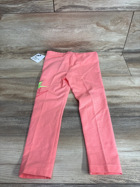 Flat lay of pink toddler Nike leggings showcasing neon green and red Nike logo on left leg with wood floor background