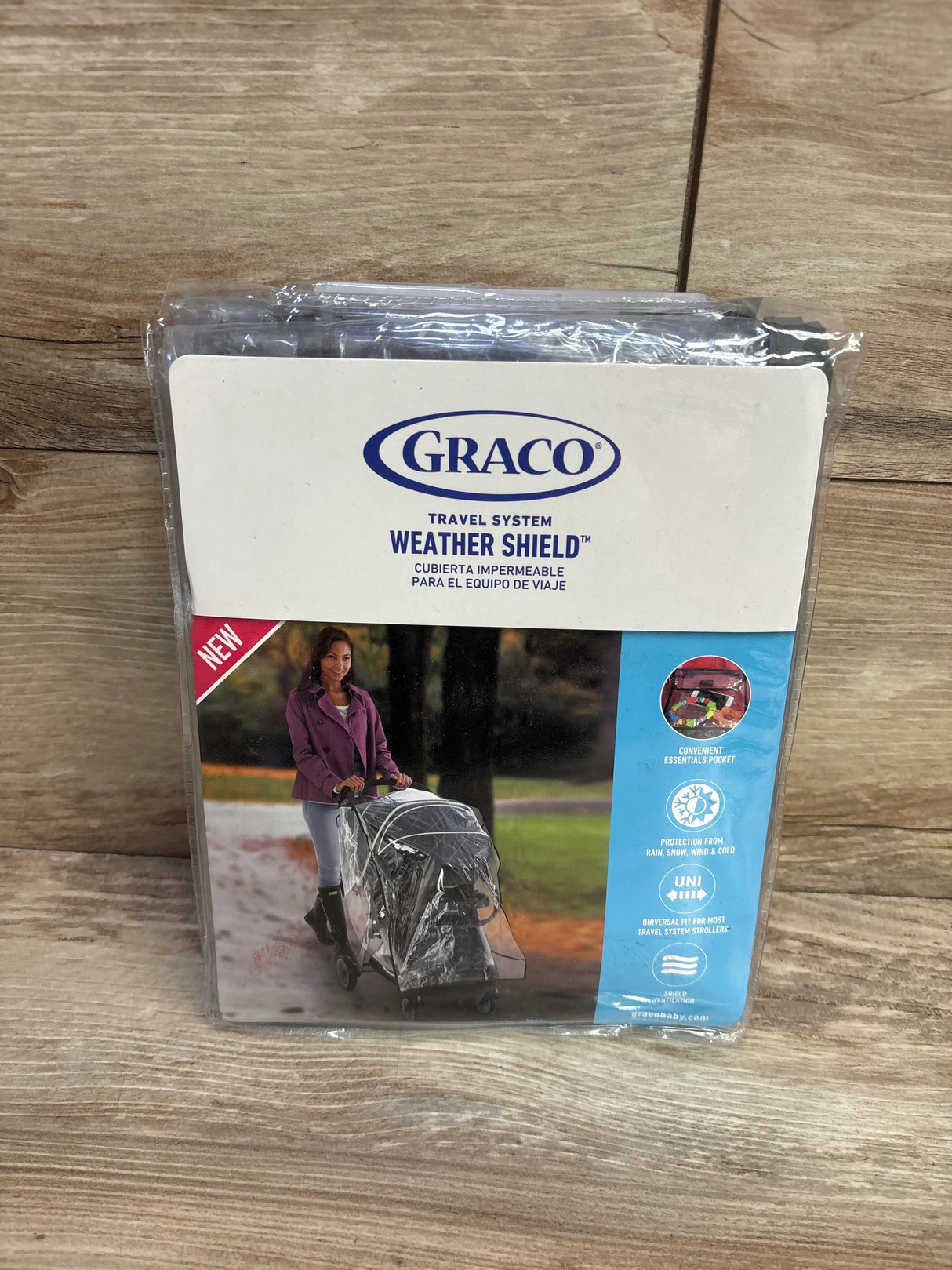Front view of Graco Travel System Weather Shield packaging showcasing clear stroller rain cover image and Graco logo on wooden background