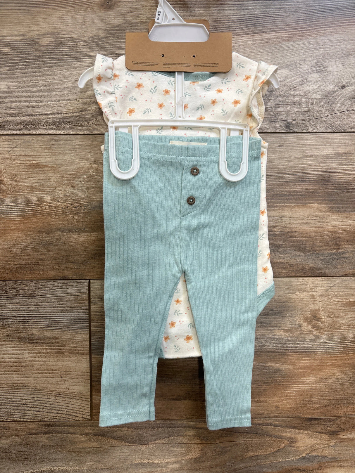 Front of 3-piece baby set, ivory floral bodysuit, mint ribbed pants with two buttons, matching headband on wood background