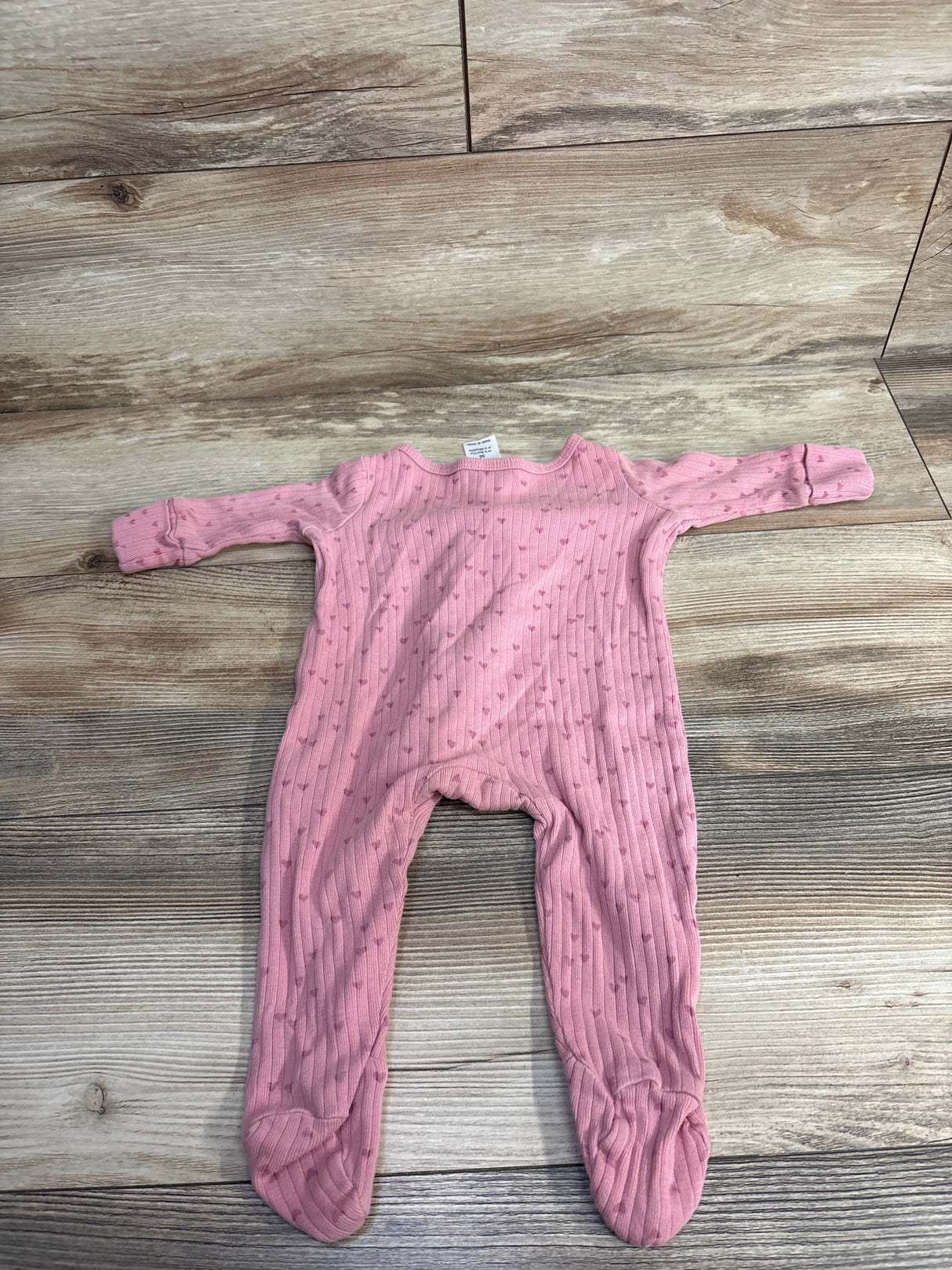 Pink ribbed baby onesie with long sleeves and feet, featuring small heart patterns, laid flat on wooden floor
