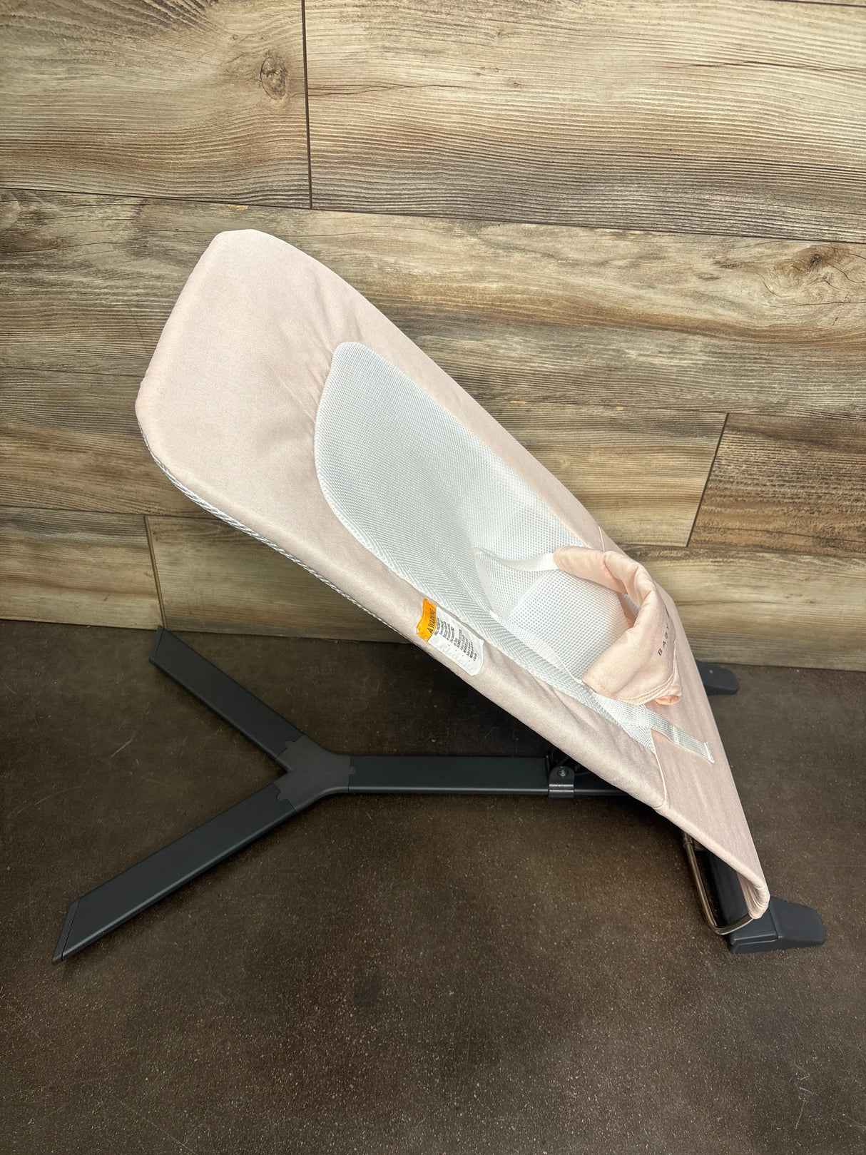 Side view of Baby Delight Alpine Deluxe bouncer in pink showing white mesh seat insert and black tripod base on wood floor