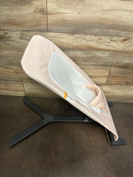 Side view of Baby Delight Alpine Deluxe bouncer in pink showing white mesh seat insert and black tripod base on wood floor