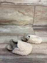Angled view of Child of Mine slip-on baby clog size 2C showing beige curly faux-sherpa upper and elastic heel strap on light wood background