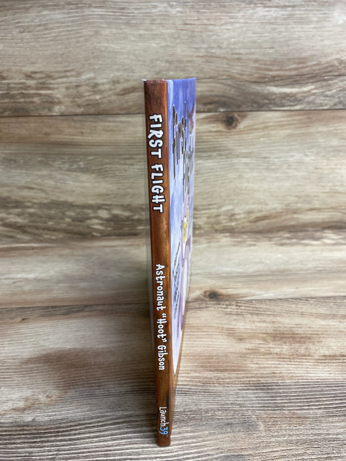 Children's book titled First Flight by Astronaut Hoot Gibson standing on wooden surface