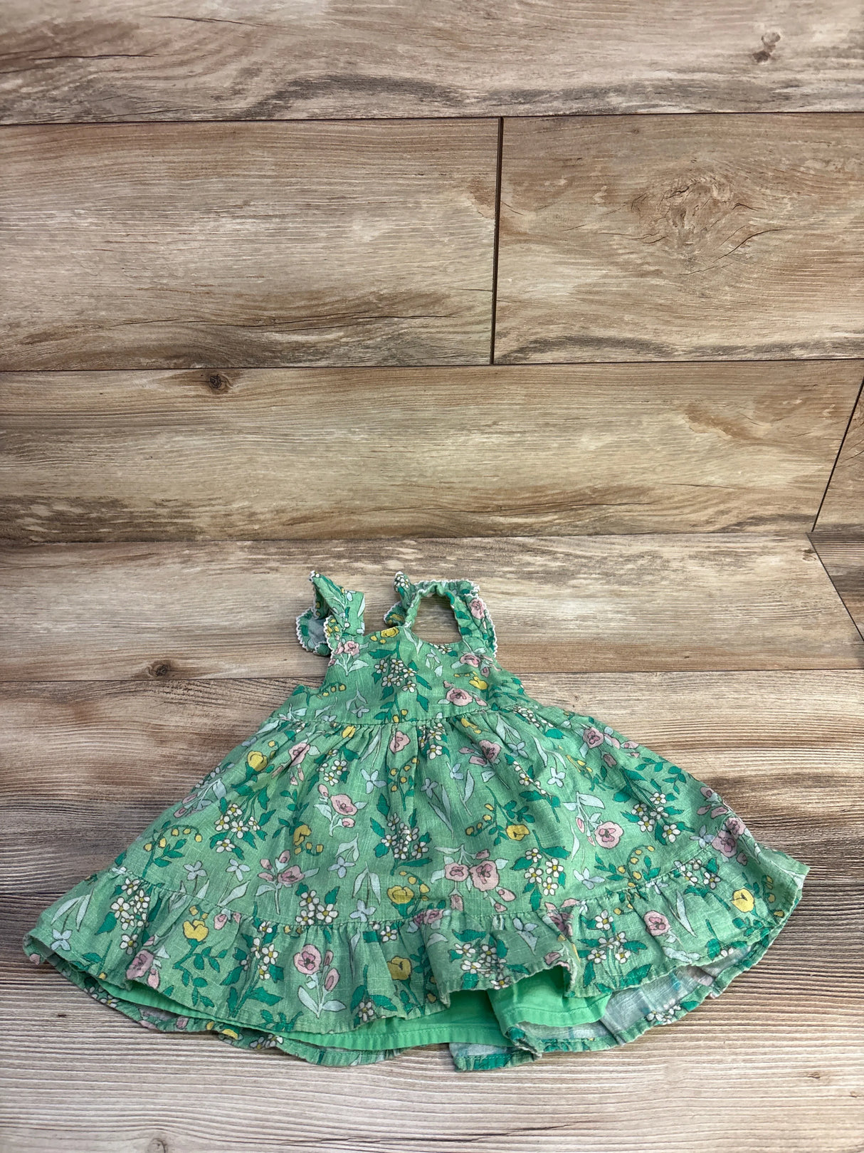 Flat lay of Cat and Jack green floral tank dress showing ruffled hem, tiered skirt and ruffled straps on wood background