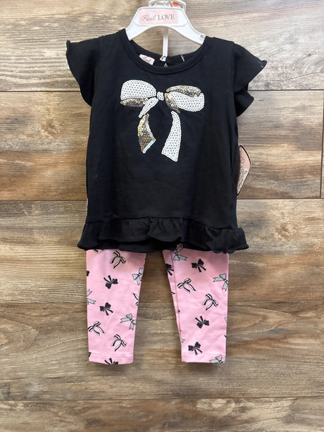 Front view of Real Love two piece shirt and pants set with black ruffled top, sequin bow, and pink bow print pants on wood background
