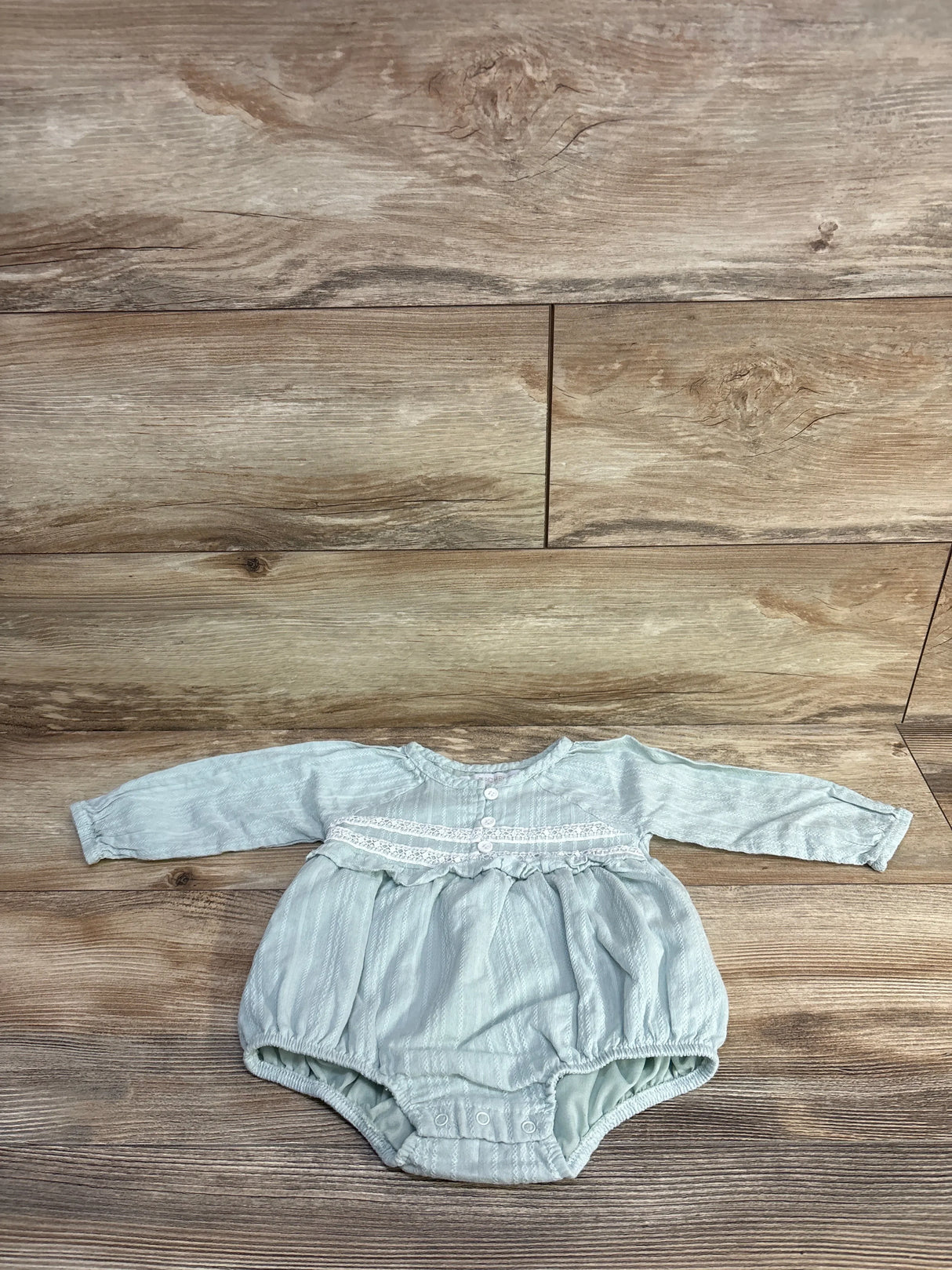 Front flat lay of green bubble romper 6-9m showing long sleeves, lace yoke and snap crotch on wood background
