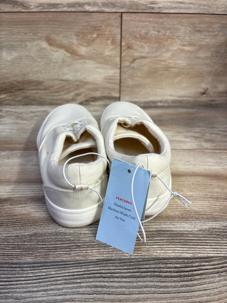 Rear view of off-white Tyler slip-on toddler sneakers showing elastic laces and attached tag on wood background