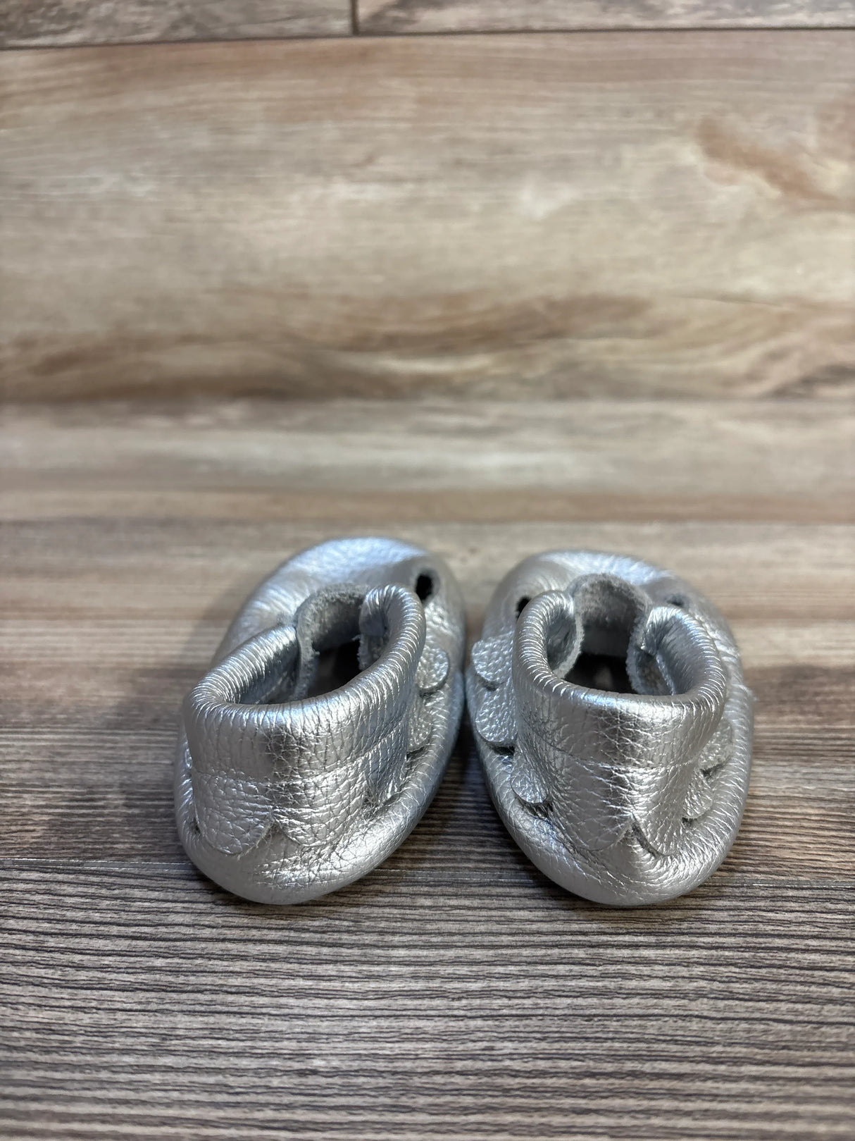Silver leather baby moccasins on wood background, gently used infant shoes
