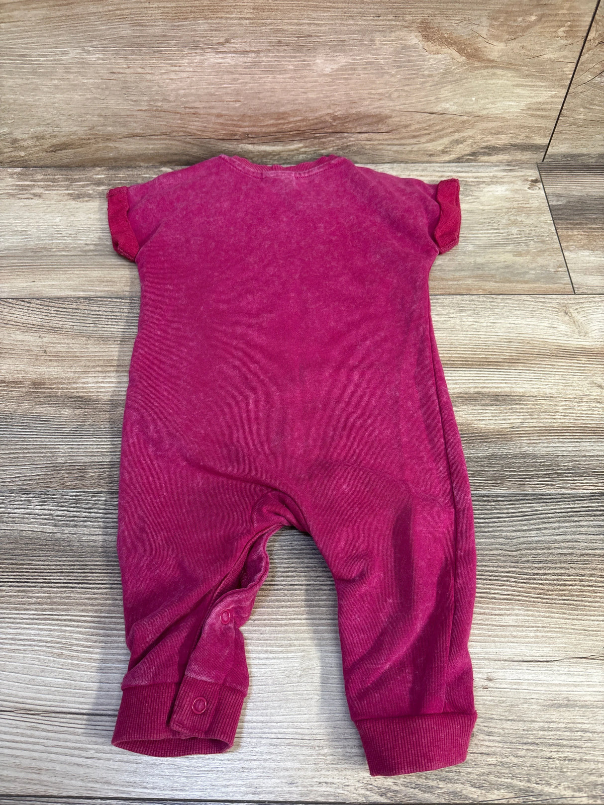 Flat-lay of pink Disney baby romper size 6-9m showcasing short sleeves, snap leg closures, faded velour texture on wood background