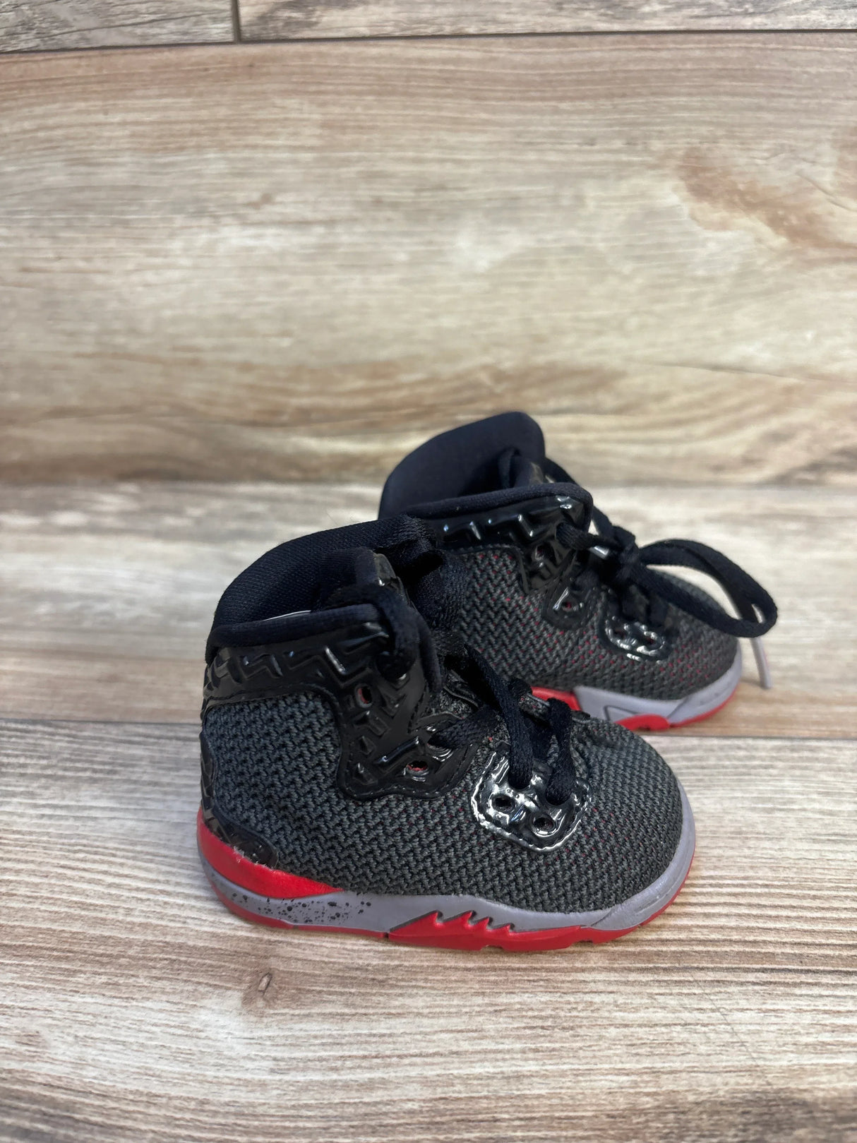 Black and red toddler sneakers with mesh upper and glossy accents on wood floor