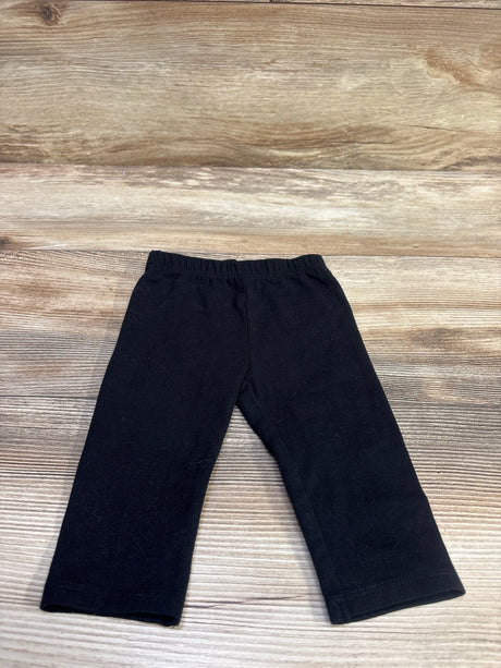 Front view of First Impressions black leggings in size 3 to 6 months showcasing elastic waistband on a wood-grain background