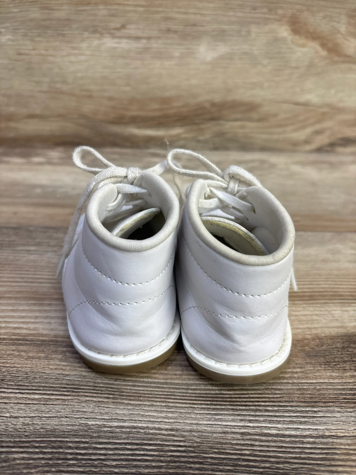 Rear view of white Teeny Toes first walker shoes showing padded ankle collars and lace-up ties on woodgrain background