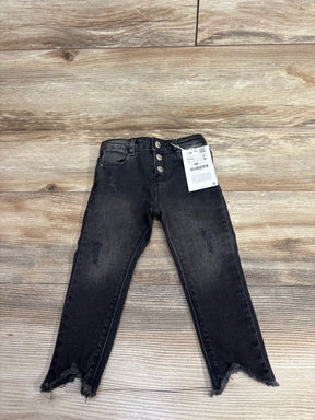 Black distressed kids jeans with three buttons and frayed hems laid flat on wooden surface