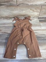 Flat lay of brown sleeveless baby jumpsuit with tied shoulder bows and snap-crotch closure on wood plank background