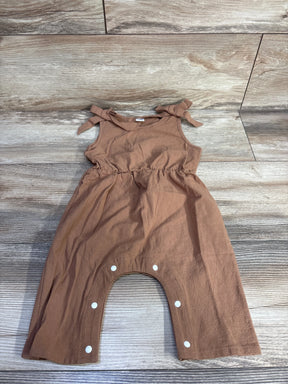 Flat lay of brown sleeveless baby jumpsuit with tied shoulder bows and snap-crotch closure on wood plank background