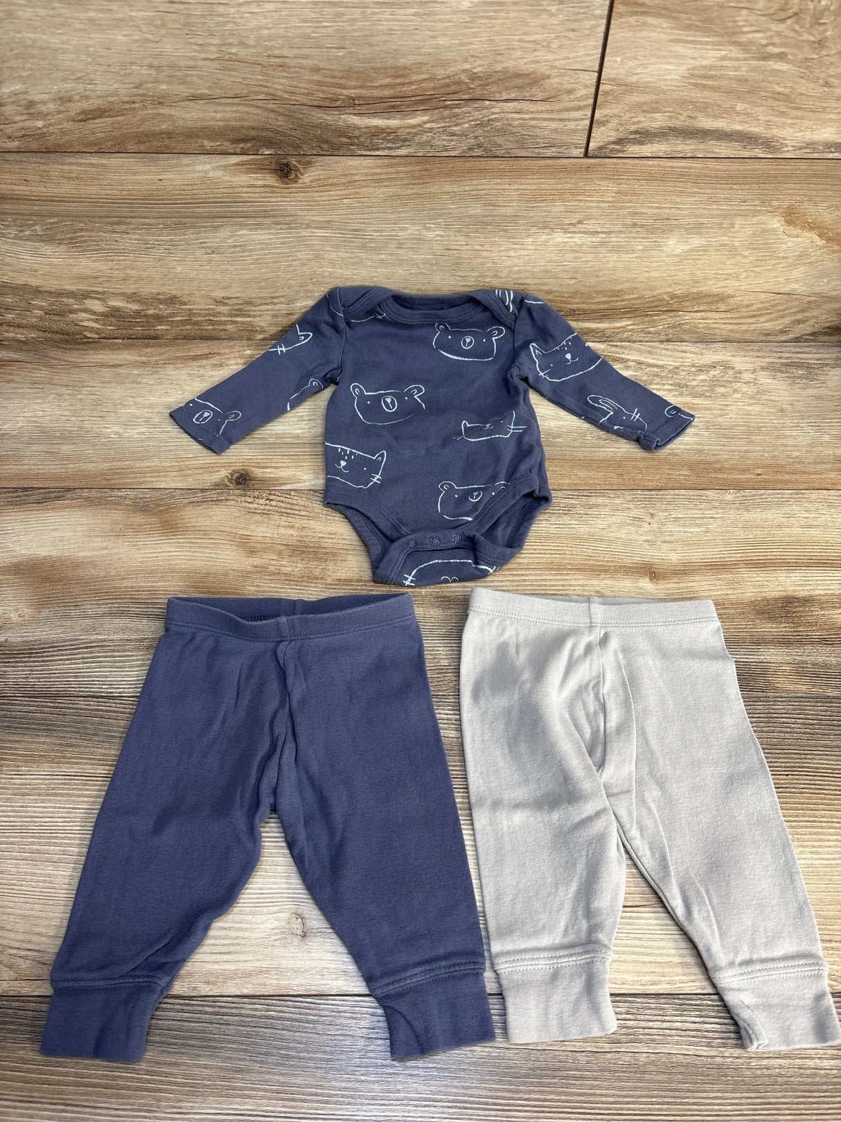 Flat lay of Cloud Island 3-piece newborn set showing navy animal-print long-sleeve bodysuit with navy and gray pants on wood floor