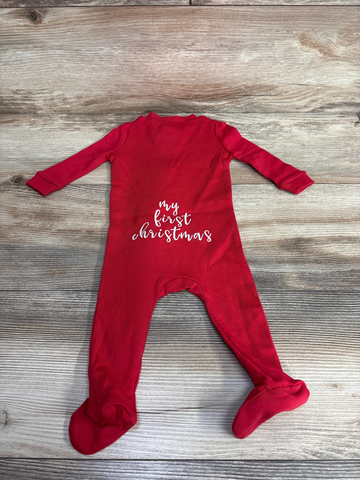 Red baby sleeper with 'my first christmas' text, footed, on wooden background