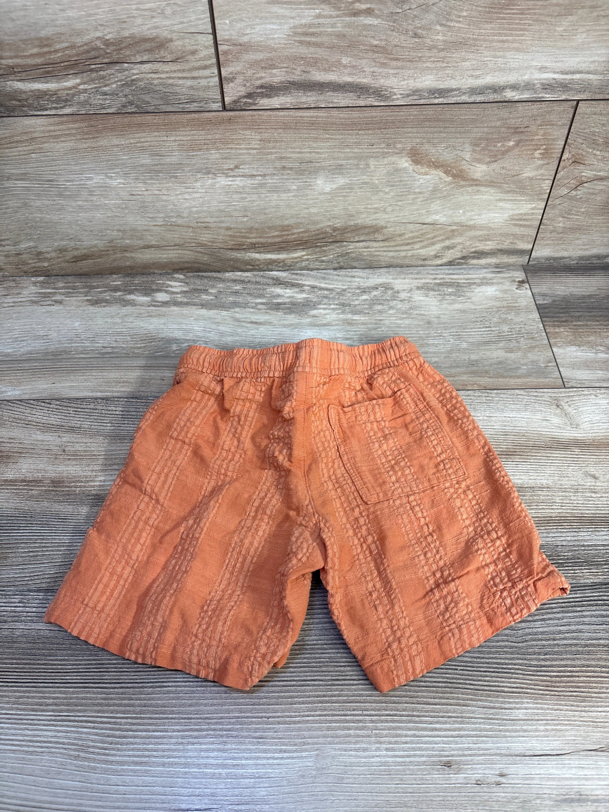 Flat lay of orange Cat & Jack toddler drawstring textured shorts with elastic waistband, back patch pocket on wood floor