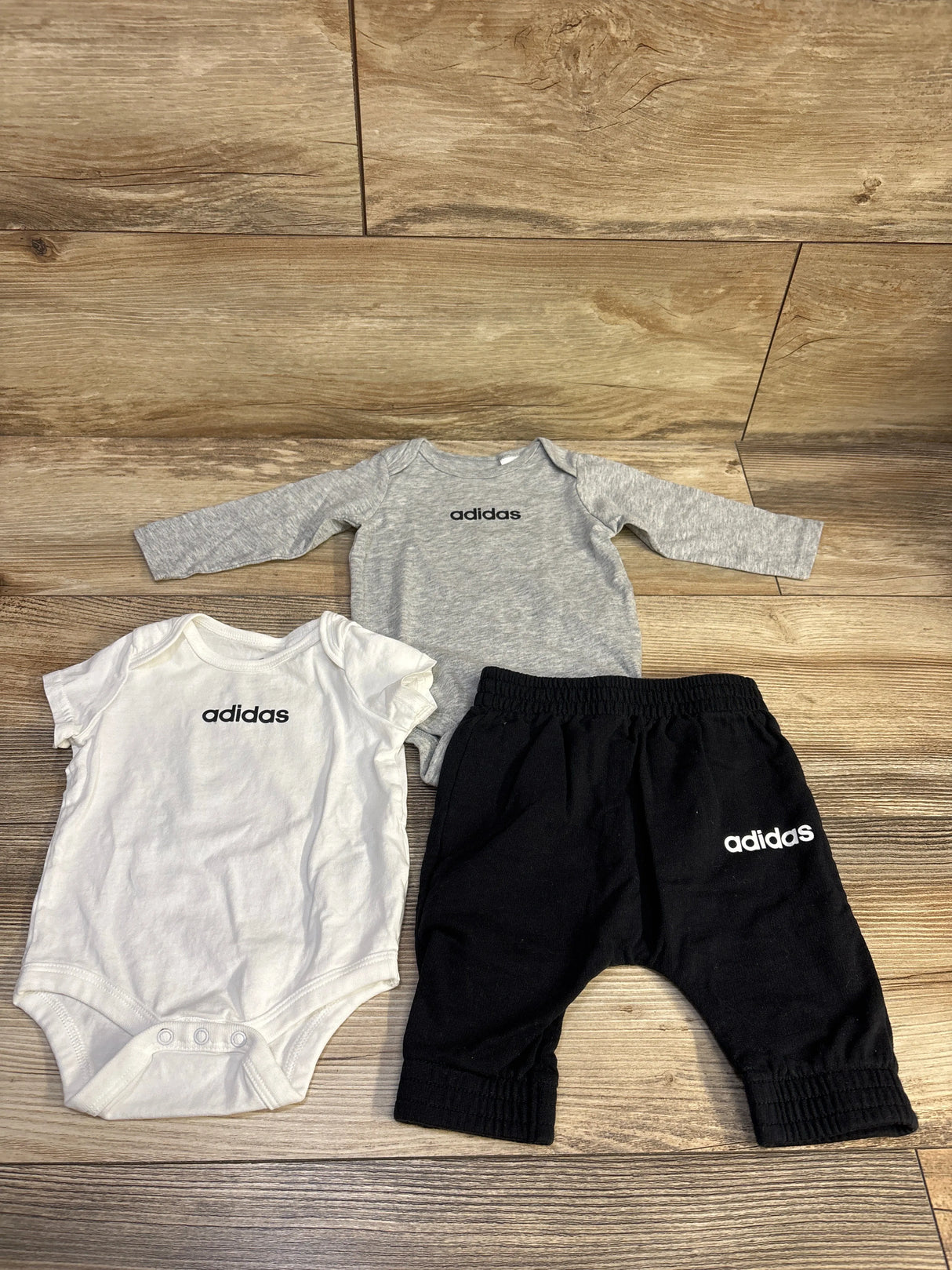 Top view of Adidas 3pc bodysuit set showcasing gray long-sleeve and white short-sleeve bodysuits with black pants