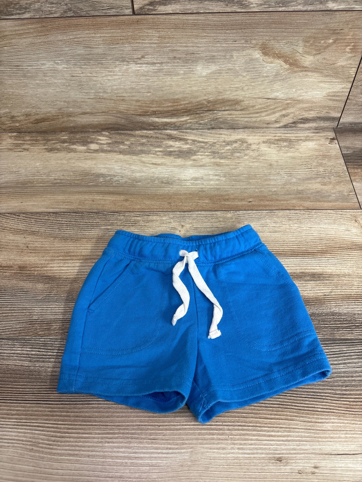 Front view of Cat & Jack toddler blue drawstring shorts showcasing elastic waistband, white drawstring and front pockets on wood background