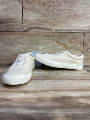 Pair of cream-colored kids canvas sneakers with white soles on a wooden floor
