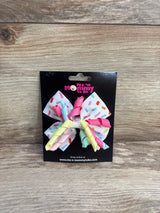 Front view of birthday hair bow with white sprinkle-patterned loops and pastel twisted ribbons on black display card on wood background