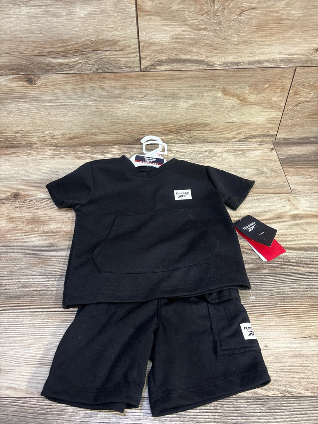 Flat-lay of black Reebok 2T shirt and shorts set showing front kangaroo pocket and Reebok logo patch on wood background